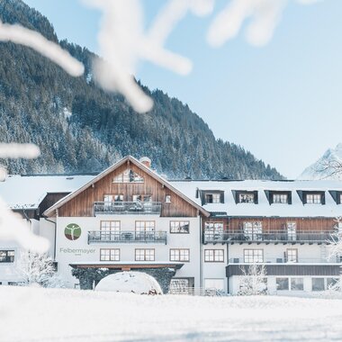 Ein charmantes Hotel im Winter, umgeben von schneebedeckten Bergen. Der klare Himmel und die schneebedeckte Landschaft schaffen eine ruhige Atmosphäre.
