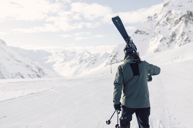 Skifahrer in olivgrüner Jacke steht auf präparierter Piste und trägt Skier auf der Schulter, Blick auf ein weites verschneites Tal, das Valzifenztal in Gargellen im Montafon.  | © Gargellner Bergbahnen GmbH & Co KG, Daniel Zangerl