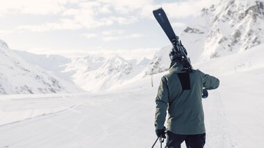 Skifahrer in olivgrüner Jacke steht auf präparierter Piste und trägt Skier auf der Schulter, Blick auf ein weites verschneites Tal, das Valzifenztal in Gargellen im Montafon.  | © Gargellner Bergbahnen GmbH & Co KG, Daniel Zangerl