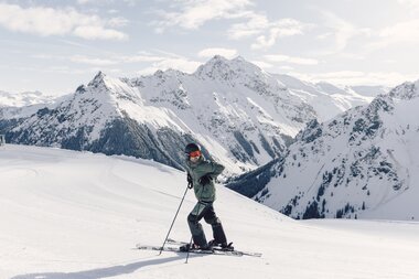 Skifahrer in olivgrüner Jacke steht auf einer präparierten Piste vor einem verschneiten Panorama im Hintergrund ist der verschneite Schmelzberggipel zu sehen.  | © Gargellner Bergbahnen GmbH & Co KG, Daniel Zangerl