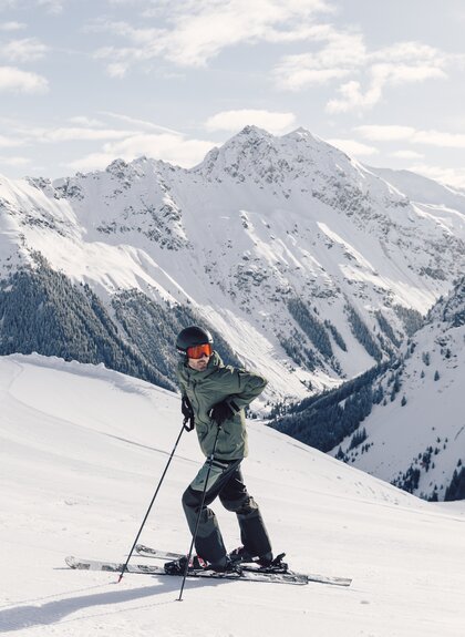 Skifahrer in olivgrüner Jacke steht auf einer präparierten Piste vor einem verschneiten Panorama im Hintergrund ist der verschneite Schmelzberggipel zu sehen.  | © Gargellner Bergbahnen GmbH & Co KG, Daniel Zangerl