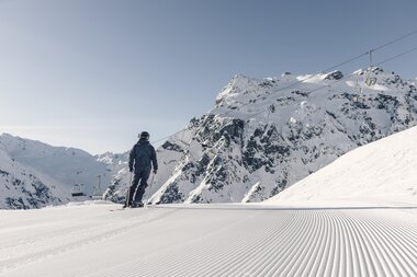 Ein Skifahrer steht auf einer frisch präparierten Piste in Gargellen mit Blick auf verschneite Berge und Sessellift. | © Gargellner Bergbahnen, Daniel Zangerl
