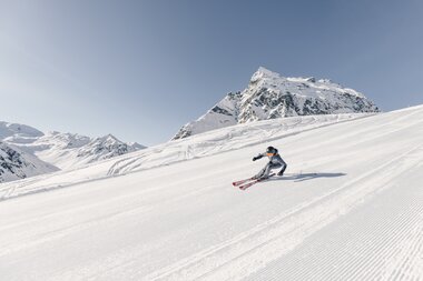 Skifahrer fährt in Schwüngen eine frisch präparierte Piste in Gargellen hinunter, verschneite Bergkulisse im Hintergrund. | © Gargellner Bergbahnen, Daniel Zangerl