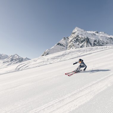 Skifahrer fährt in Schwüngen eine frisch präparierte Piste in Gargellen hinunter, verschneite Bergkulisse im Hintergrund. | © Gargellner Bergbahnen, Daniel Zangerl