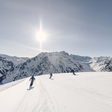 Drei Skifahrer fahren eine breite, frisch präparierte Piste in Gargellen bei Sonnenschein mit Bergpanorama im Hintergrund. | © Gargellner Bergbahnen GmbH & Co KG, Daniel Zangerl