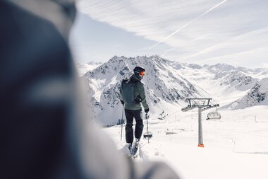 Skifahrer mit Helm und Rucksack steht auf einer Piste in Gargellen und blickt ins verschneite Tal, Sessellift im Hintergrund. | © Gargellner Bergbahnen GmbH & Co KG, Daniel Zangerl