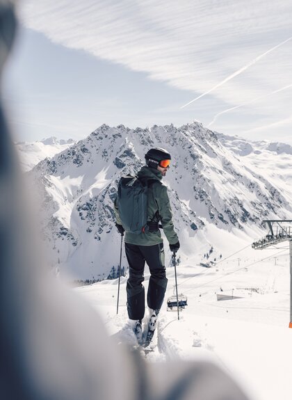 Skifahrer mit Helm und Rucksack steht auf einer Piste in Gargellen und blickt ins verschneite Tal, Sessellift im Hintergrund. | © Gargellner Bergbahnen GmbH & Co KG, Daniel Zangerl