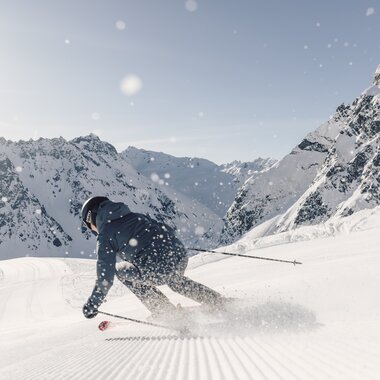 Skifahrer fährt dynamisch eine frisch präparierte Piste in Gargellen hinunter, Schneespritzer in der Luft, Berge im Hintergrund. | © Gargellner Bergbahnen GmbH & Co KG, Daniel Zangerl
