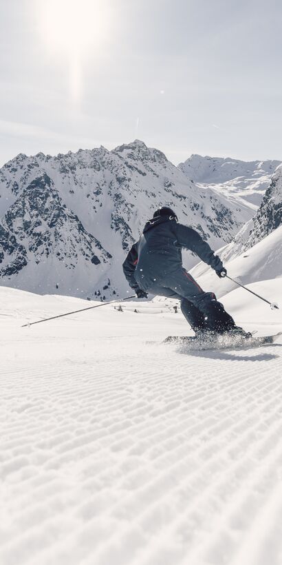 Skifahrer fährt in Schwüngen eine frisch präparierte Piste in Gargellen hinunter, verschneite Bergkulisse im Hintergrund. | © Gargellner Bergbahnen GmbH & Co KG, Daniel Zangerl
