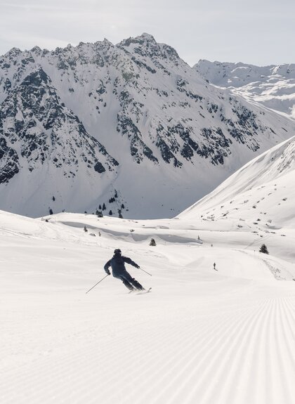Skifahrer fährt in Schwüngen eine frisch präparierte Piste in Gargellen hinunter, verschneite Bergkulisse im Hintergrund. | © Gargellner Bergbahnen GmbH & Co KG, Daniel Zangerl