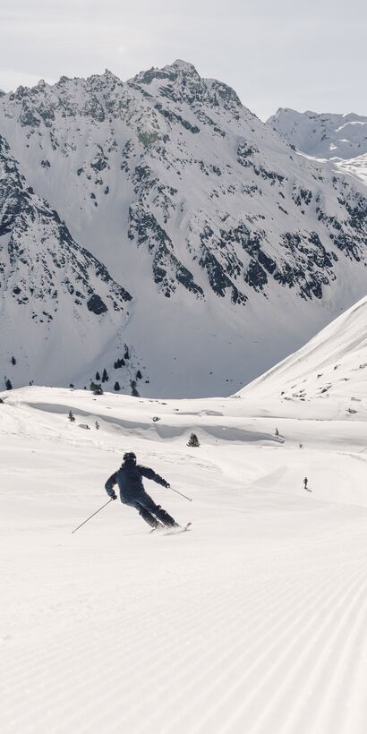 Skifahrer fährt in Schwüngen eine frisch präparierte Piste in Gargellen hinunter, verschneite Bergkulisse im Hintergrund. | © Gargellner Bergbahnen GmbH & Co KG, Daniel Zangerl