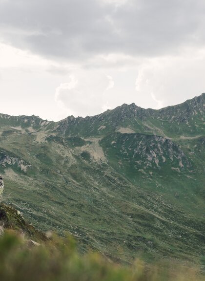 Wanderer steht auf einem Felsen in Gargellen und blickt über die grünen Bergketten. | © Gargellner Bergbahnen GmbH & Co KG, Daniel Zangerl