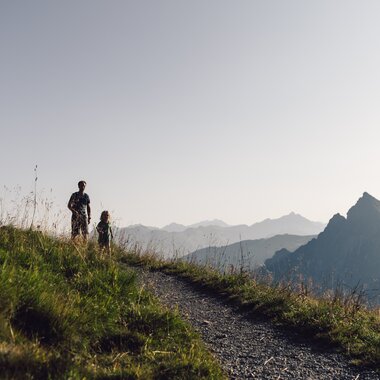 Vater und Kind wandern auf einem Bergpfad in Gargellen bei Abendsonne, Wegweiser am Wegrand. | © Gargellner Bergbahnen GmbH & Co KG, Daniel Zangerl