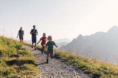 Familie mit zwei Kindern wandert und läuft lachend auf einem Bergpfad in Gargellen bei Sonnenschein. | © Gargellner Bergbahnen GmbH & Co KG, Daniel Zangerl
