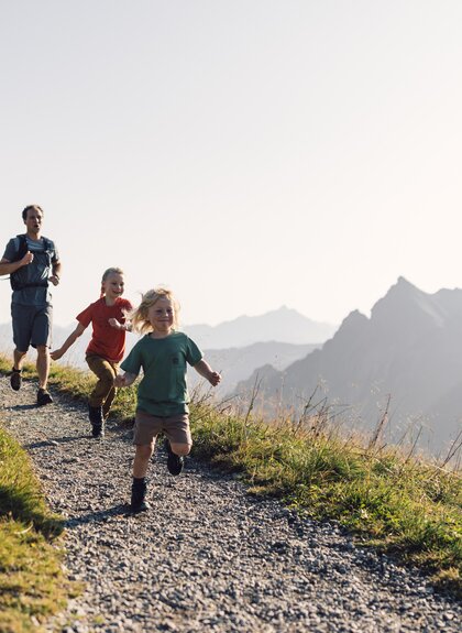 Familie mit zwei Kindern wandert und läuft lachend auf einem Bergpfad in Gargellen bei Sonnenschein. | © Gargellner Bergbahnen GmbH & Co KG, Daniel Zangerl