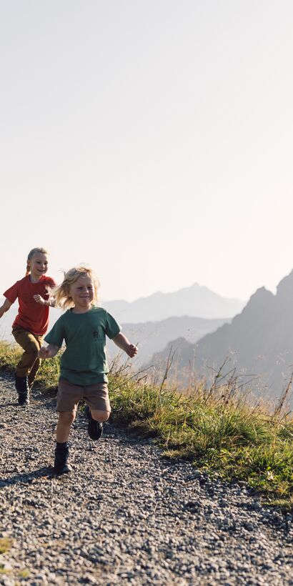 Familie mit zwei Kindern wandert und läuft lachend auf einem Bergpfad in Gargellen bei Sonnenschein. | © Gargellner Bergbahnen GmbH & Co KG, Daniel Zangerl