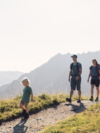 Eine Familie mit zwei Kindern wandert auf einem sonnigen Bergpfad am Gargellner Schafberg Weg, umgeben von beeindruckenden Berggipfeln. | © Gargellner Bergbahnen GmbH & Co KG, Daniel Zangerl