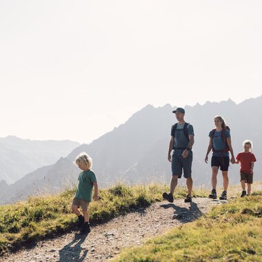 Eine Familie mit zwei Kindern wandert auf einem sonnigen Bergpfad am Gargellner Schafberg Weg, umgeben von beeindruckenden Berggipfeln. | © Gargellner Bergbahnen GmbH & Co KG, Daniel Zangerl