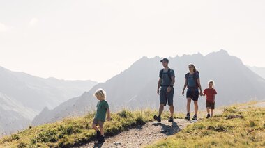 Eine Familie mit zwei Kindern wandert auf einem sonnigen Bergpfad am Gargellner Schafberg Weg, umgeben von beeindruckenden Berggipfeln. | © Gargellner Bergbahnen GmbH & Co KG, Daniel Zangerl