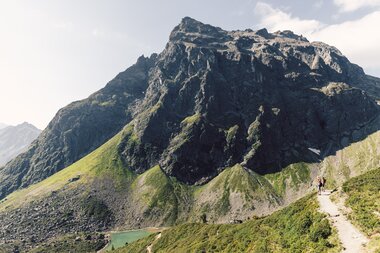 ine Familie wandert auf einem schmalen Bergpfad am Gargellner Schafberg. Im Hintergrund ragt die beeindruckende Madrisa mit ihren steilen, felsigen Flanken und grünen Wiesenhängen in den Himmel. | © Gargellner Bergbahnen GmbH & Co KG, Daniel Zangerl