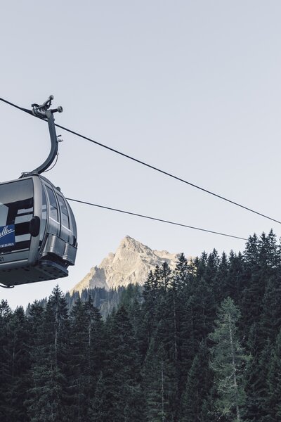 ine silberne Gondel der Gargellner Bergbahnen schwebt über einen dichten Nadelwald in Richtung Bergstation. Im Hintergrund ragt der Gipfel der Madrisa in der Abendsonne auf, während der Himmel klar und hellblau ist. | © Gargellner Bergbahnen GmbH & Co KG, Daniel Zangerl