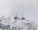 Zwei Gondeln der Schafbergbahn in Gargellen schweben vor einer beeindruckenden, schneebedeckten Bergkulisse. Die modernen Kabinen der Gargellner Bergbahnen heben sich klar vom hellen Winterhimmel ab, während im Hintergrund die majestätischen Gipfel der Montafoner Alpen aufragen. | © Gargellner Bergbahnen GmbH & Co KG, Daniel Zangerl