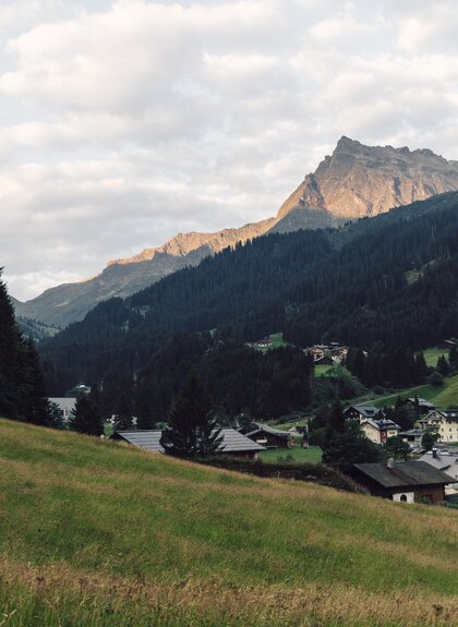 Blick über das Bergdorf Gargellen mit grünen Wiesen, bewaldeten Berghängen und den umliegenden Gipfeln im Abendlicht. | © Gargellner Bergbahnen GmbH & Co, KG, Daniel Zangerl