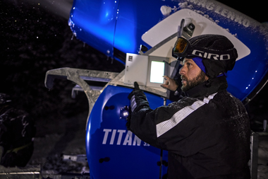 Zwei Mitarbeiter der Gargellner Bergbahnen überwachen nachts eine laufende Schneekanone. Die Maschine sprüht feinen, künstlichen Schnee über die beleuchtete Skipiste, während im Hintergrund schneebedeckte Bäume im Dunkeln stehen. Die Szene ist von kaltem, bläulichem Licht erhellt und zeigt die präzise Arbeit im nächtlichen Skigebiet. | © Gargellner Bergbahnen GmbH & Co KG, Stefan Kothner