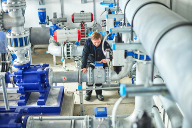 Ein Mitarbeiter der Gargellner Bergbahnen überprüft in der Pumpstation die Steuerung einer Leitung. Umgeben von großen silbernen Rohren, blauen Ventilen und Pumpen führt er Wartungsarbeiten an der Beschneiungsanlage durch. | © Gargellner Bergbahnen GmbH & Co KG, Stefan Kothner