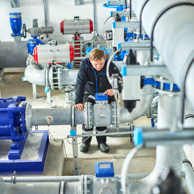 Ein Mitarbeiter der Gargellner Bergbahnen überprüft in der Pumpstation die Steuerung einer Leitung. Umgeben von großen silbernen Rohren, blauen Ventilen und Pumpen führt er Wartungsarbeiten an der Beschneiungsanlage durch. | © Gargellner Bergbahnen GmbH & Co KG, Stefan Kothner