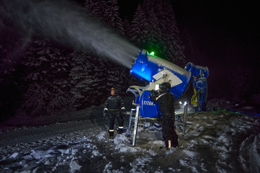 Zwei Mitarbeiter der Gargellner Bergbahnen überwachen nachts eine laufende Schneekanone. Die Maschine sprüht feinen, künstlichen Schnee über die beleuchtete Skipiste, während im Hintergrund schneebedeckte Bäume im Dunkeln stehen. Die Szene ist von kaltem, bläulichem Licht erhellt und zeigt die präzise Arbeit im nächtlichen Skigebiet. | © Gargellner Bergbahnen GmbH & Co KG, Stefan Kothner
