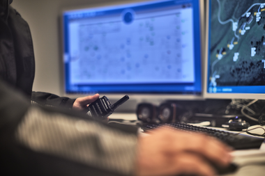 Eine Mitarbeiterin oder ein Mitarbeiter der Gargellner Bergbahnen überwacht die Schneianlage über zwei große Bildschirme im Kontrollraum. Auf einem Monitor ist ein digitales Geländemodell zu sehen, auf dem anderen technische Daten. In der Hand hält die Person ein Funkgerät, um mit dem Team auf der Piste zu kommunizieren. | © Gargellner Bergbahnen GmbH & Co KG, Stefan Kothner