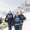 Drei Mitglieder der Pistenrettung Gargellen stehen gemeinsam im Schnee, bereit für ihren nächsten Einsatz. Hinter ihnen ein Schneemobil mit Rettungsschlitten, im Hintergrund die verschneiten Gipfel des Montafons. Ihre Entschlossenheit und Professionalität prägen das Bild – Sicherheit steht an erster Stelle. | © Gargellner Bergbahnen GmbH & Co KG, Daniel Zangerl