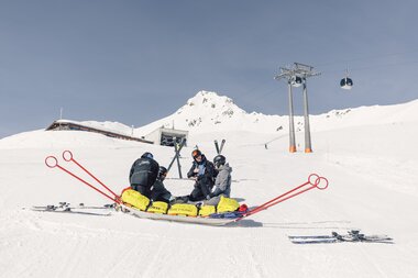 Mitarbeitende der Pistenrettung leisten Erste Hilfe auf der Skipiste in Gargellen. Eine verletzte Person wird versorgt, während im Hintergrund die Bergbahn und verschneite Gipfel zu sehen sind. | © Gargellner Bergbahnen GmbH & Co KG, Daniel Zangerl