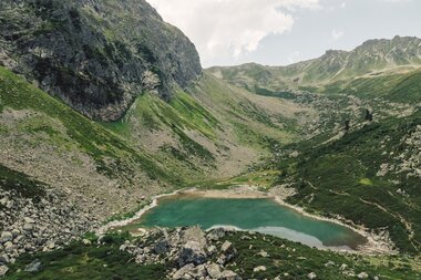 Blick auf den türkisblauen Gandasee, eingebettet in eine raue, grüne Berglandschaft oberhalb von Gargellen. Der stille See spiegelt die umliegenden Gipfel und vermittelt ein Gefühl von unberührter Natur und alpiner Ruhe – ein verstecktes Juwel im Montafon. | © Gargellner Bergbahnen GmbH & Co KG, Daniel Zangerl