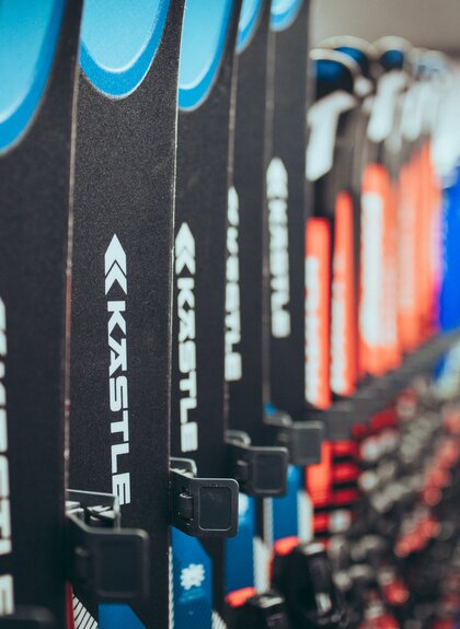 Mehrere Paar Ski der Marke Kästle stehen ordentlich in einer Reihe in einem Skiverleih. Die Vorderseiten der Ski in Blau, Schwarz und Rot sind deutlich zu erkennen. Der Hintergrund des Raums ist unscharf, wodurch der Fokus auf den Ski liegt. | © Gargellner Bergbahnen GmbH & Co KG, Christoph Schöch 