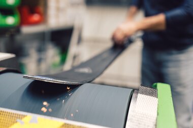 Detailaufnahme einer Skispitze während des Schleifens im Skiservice des PME Shop & Rent; der Ski wird über eine rotierende Schleiffläche geführt, dabei entstehen Funken an der Metallkante. | © Gargellner Bergbahnen GmbH & Co KG, Daniel Zangerl