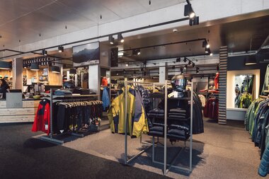 Großzügiger Innenbereich des PME Shop & Rent mit mehreren Kleiderständern und Präsentationsflächen für Wintersportbekleidung; Jacken, Hosen und Accessoires sind geordnet ausgestellt, im Hintergrund sind Kassenbereich und weitere Shopbereiche sichtbar. | © Gargellner Bergbahnen GmbH & Co KG, Daniel Zangerl