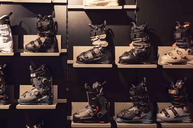 Mehrere Skischuhe verschiedener Modelle stehen geordnet auf Regalböden im Innenbereich des PME Shop & Rent; die Schuhe sind frontal sichtbar und dienen der Auswahl für Verkauf oder Verleih. | © Gargellner Bergbahnen GmbH & Co KG, Daniel Zangerl