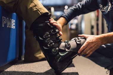 Detailaufnahme eines Skischuhs während der Anpassung im PME Shop & Rent; ein Mitarbeiter justiert den Skischuh am Fuß eines Kunden, die Schnallen und der Schaft des Skischuhs sind deutlich sichtbar. | © Gargellner Bergbahnen GmbH & Co KG, Daniel Zangerl