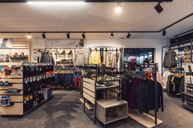 Der Innenraum eines Sportshops mit übersichtlich angeordneten Regalen und Ständern für Wintersportbekleidung, Helme, Handschuhe und Accessoires; Jacken und Hosen hängen sortiert nach Kategorien. | © Gargellner Bergbahnen GmbH & Co KG, Daniel Zangerl