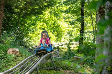 Eine Frau und ein Kind fahren auf einer Sommerrodelbahn durch den Wald hinunter | © Golm Silvretta Lünersee Tourismus GmbH Bregenz, Stefan Kothner