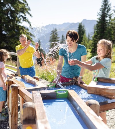 Vater und Mutter, die gemeinsam mit ihren zwei Töchtern beim Wasserspiel auf Golmis Forschungspfad die Kraft des Wassers entdecken | © Golm Silvretta Lünersee Tourismus GmbH Bregenz, Stefan Kothner