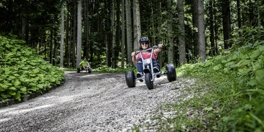 Freunde die mit Mountaincarts den Berg hinunter auf einer Schotterstraße hinunter fahren | © Mountaincart GmbH
