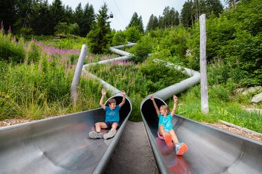 Zwei Kinder die gerade aus zwei einzelnen Rutschen am Waldrutschenpark-Golm rutschen | © Golm Silvretta Lünersee Tourismus GmbH Bregenz, Mathäus Gartner